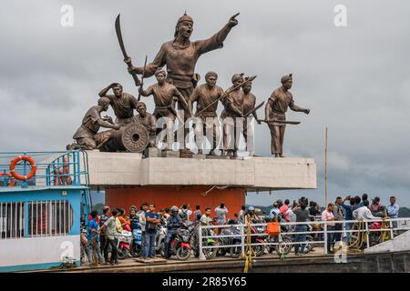 Guwahati, Indien. 17. Juni 2023. Die Menschen fahren in einer Fähre, während dunkle Wolken über der Statue von Lachit Borphukan schweben, dem Kommandanten des Ahom-Königreichs am Brahmaputra River in Guwahati. Der Wasserstand des Brahmaputra River ist aufgrund starker Regenfälle in Guwahati gestiegen. Die starken Regenfälle verursachten auch Überschwemmungen in mehreren tief liegenden Teilen der Stadt. Kredit: SOPA Images Limited/Alamy Live News Stockfoto