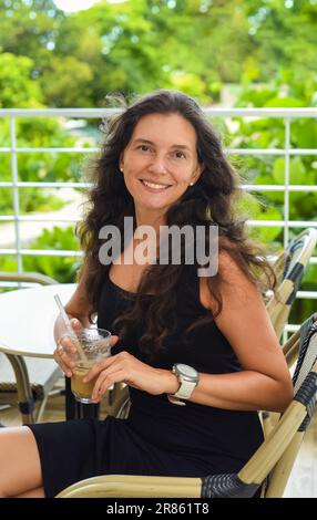 Porträt einer 39-jährigen russin, die ohne Make-up mit einem Glas Eiskaffee in schwarzem Kleid gesessen hat Stockfoto