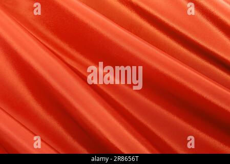 Struktur eines glatten, luxuriösen, eleganten Stoffes in Orange und Rot. Lilafarbener Satin- oder Seidenstoff mit Falten und Wellen Stockfoto