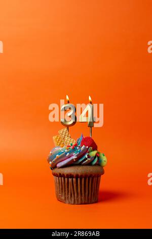 Geburtstagskuchen mit Nummer 34 - Cupcake auf orangefarbenem Hintergrund mit Geburtstagskerzen Stockfoto