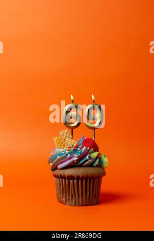 Geburtstagskuchen mit Nummer 69 - Cupcake auf orangefarbenem Hintergrund mit Geburtstagskerzen Stockfoto