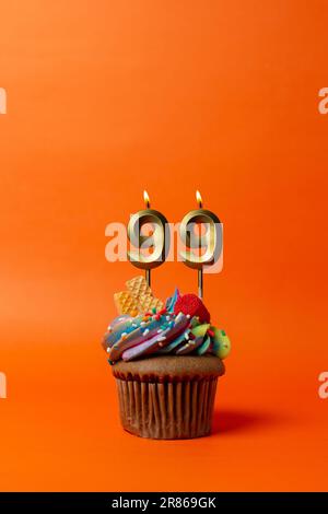 Geburtstagskuchen mit Nummer 99 - Cupcake auf orangefarbenem Hintergrund mit Geburtstagskerzen Stockfoto