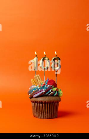 Geburtstagskuchen mit Nummer 108 - Cupcake auf orangefarbenem Hintergrund mit Geburtstagskerzen Stockfoto