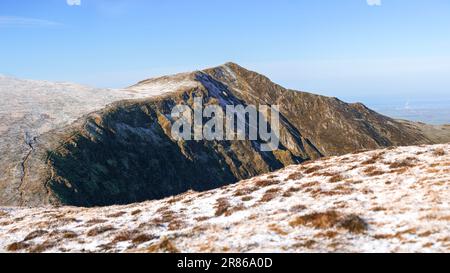 Ein entfernter Mountainbiker nähert sich dem Gipfel des Hopegill Head über Hobcarton Crags im Winter im englischen Lake District, Großbritannien. Stockfoto