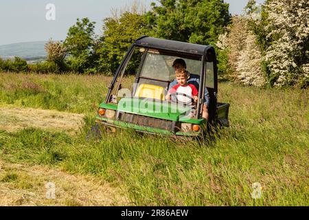 Sechs Jahre alter Junge, der einen John Deere Gator, High Bickington, North Devon, England, Großbritannien, taucht. Stockfoto