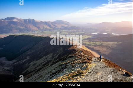 Ein Mountainbiker, der die Aussicht auf dem Weg bis zum Gipfel des Grisedale Pike mit Skiddaw und Blencathra in der Ferne im Winter im Engl genießt Stockfoto