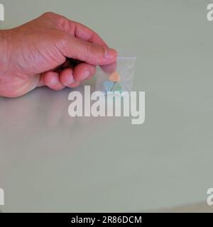 Hand hält einen Beutel mit Tesla Ecstasy-Pillen in Orange, Grün und Blau, die wie ein Schild mit dem Tesla Logo geformt sind; MDMA Molly für die Freizeit. Stockfoto