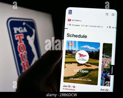Person, die ein Mobiltelefon mit der Webseite der US-Golforganisation PGA Tour auf dem Bildschirm vor dem Logo hält. Konzentrieren Sie sich auf die Mitte des Telefondisplays. Stockfoto