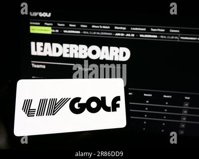 Person mit Handy mit Logo der Sportorganisation LIV Golf auf dem Bildschirm vor der Webseite. Konzentrieren Sie sich auf das Display des Telefons. Stockfoto