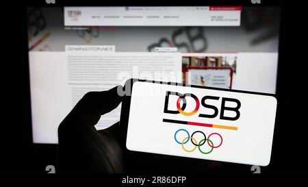 Person, die ein Mobiltelefon mit dem Logo der Organisation Deutscher Olympischer Sportbund (DOSB) auf dem Bildschirm vor der Webseite hält. Konzentrieren Sie sich auf das Display des Telefons. Stockfoto