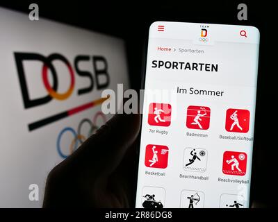 Person, die ein Mobiltelefon mit einer Webseite der Organisatin Deutscher Olympischer Sportbund (DOSB) auf dem Bildschirm mit Logo hält. Konzentrieren Sie sich auf die Mitte des Telefondisplays. Stockfoto
