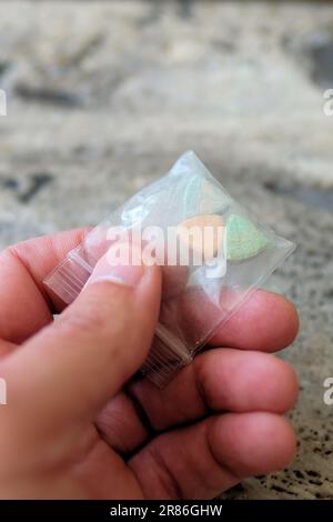Hand hält Tesla Ecstasy-Pillen in Orange, Grün und Blau, die wie ein Schild mit dem Tesla Logo geformt sind; 240 Milligramm Freizeit-MDMA. Stockfoto