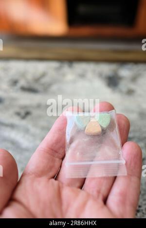 Hand hält Tesla Ecstasy-Pillen in Orange, Grün und Blau, die wie ein Schild mit dem Tesla Logo geformt sind; 240 Milligramm Freizeit-MDMA. Stockfoto