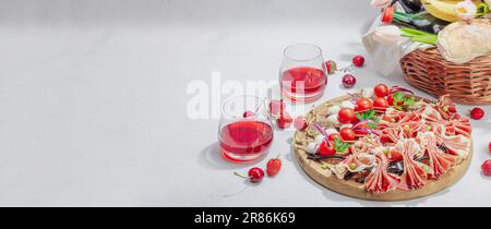 Picknick-Food-Konzept. Korb mit Wein und Baguette, Snacks auf Spießen. Fleisch, Käse, Gemüse, Obst und Blumenstrauß. Hartes Licht, dunkle s Stockfoto