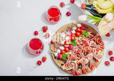 Picknick-Food-Konzept. Korb mit Wein und Baguette, Snacks auf Spießen. Fleisch, Käse, Gemüse, Obst und Blumenstrauß. Hartes Licht, dunkle s Stockfoto