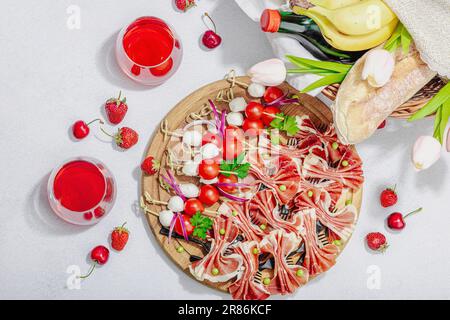 Picknick-Food-Konzept. Korb mit Wein und Baguette, Snacks auf Spießen. Fleisch, Käse, Gemüse, Obst und Blumenstrauß. Hartes Licht, dunkle s Stockfoto