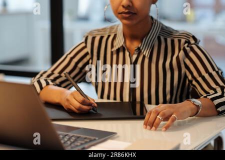 Konzentrieren Sie sich auf die Hände einer jungen afroamerikanischen Grafikdesignerin mit Eingabestift, die etwas auf dem Touchpad-Bildschirm vor dem Notebook zeichnet Stockfoto