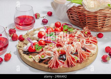 Picknick-Food-Konzept. Korb mit Wein und Baguette, Snacks auf Spießen. Fleisch, Käse, Gemüse, Obst und Blumenstrauß. Hartes Licht, dunkle s Stockfoto