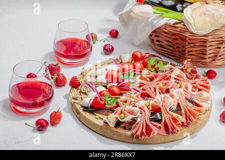 Picknick-Food-Konzept. Korb mit Wein und Baguette, Snacks auf Spießen. Fleisch, Käse, Gemüse, Obst und Blumenstrauß. Hartes Licht, dunkle s Stockfoto