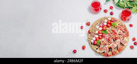 Picknick-Food-Konzept. Korb mit Wein und Baguette, Snacks auf Spießen. Fleisch, Käse, Gemüse, Obst und Blumenstrauß. Hartes Licht, dunkle s Stockfoto