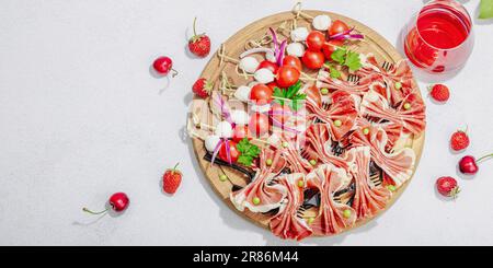 Picknick-Food-Konzept. Korb mit Wein und Baguette, Snacks auf Spießen. Fleisch, Käse, Gemüse, Obst und Blumenstrauß. Hartes Licht, dunkle s Stockfoto