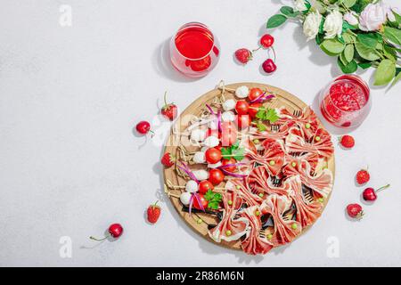 Picknick-Food-Konzept. Korb mit Wein und Baguette, Snacks auf Spießen. Fleisch, Käse, Gemüse, Obst und Blumenstrauß. Hartes Licht, dunkle s Stockfoto