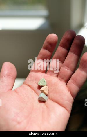 Hand hält Tesla Ecstasy-Pillen in Orange, Grün und Blau, die wie ein Schild mit dem Tesla Logo geformt sind; 240 Milligramm Freizeit-MDMA. Stockfoto