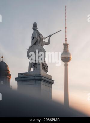 Eine majestätische Statue einer Figur mit einem Schwert steht vor einem modernen Betongebäude und ein hoher Fernsehturm im Hintergrund Stockfoto