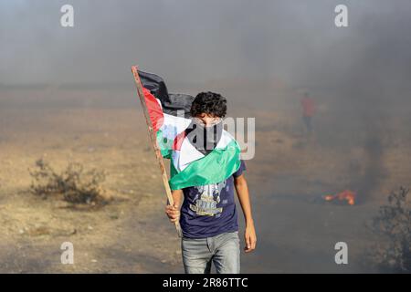 Gaza. 19. Juni 2023. Ein palästinensischer Protestteilnehmer hält eine Flagge während eines Protests gegen die Ermordung von fünf Palästinensern in der Nähe des Zauns der Grenze zwischen Gaza und Israel östlich von Gaza-Stadt am 19. Juni 2023. Palästina verurteilte am Montag die Ermordung von fünf Palästinensern durch die israelische Armee und die Verwundung Dutzender anderer während eines Überfalls in der Stadt Dschenin im nördlichen Westjordanland und ihrem Flüchtlingslager. Kredit: Rizek Abdeljawad/Xinhua/Alamy Live News Stockfoto