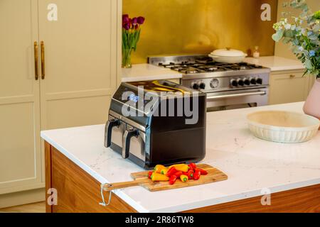 Airfryer auf der Marmorarbeitsfläche der häuslichen Kücheninsel mit einem traditionellen Gaskocher im Hintergrund. Stockfoto