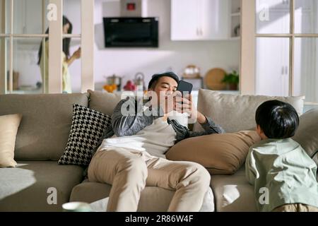 Junge asiatische Eltern, die von Smartphones abhängig sind, ignorieren das Kind, Konzept für Smartphone- oder Social-Media-sucht Stockfoto