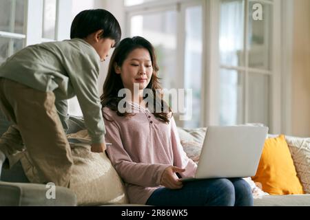 Junge asiatische Geschäftsfrau Mutter, die zu Hause arbeiten wollte, genervt von hyperaktivem Sohn Stockfoto