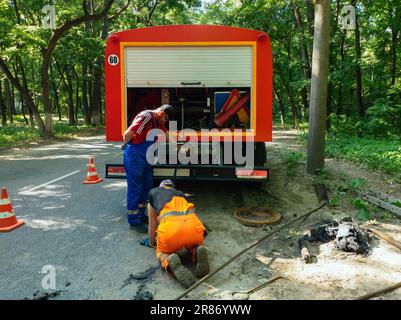 Kanalisationsarbeiter, die den Gullyschacht reinigen und die Kanalisation auf der Straße freimachen. Stockfoto