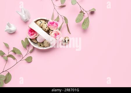 Korb mit Osterwachteleiern, Rosenblüten, Eukalyptusästen und Hasen auf rosa Hintergrund Stockfoto