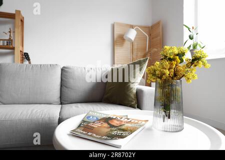 Vase mit Mimosablumen und Zeitschriften auf dem Tisch im Wohnzimmer Stockfoto