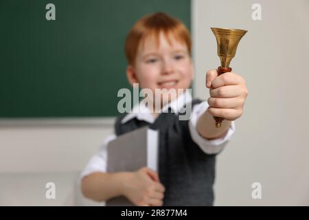 Süßer kleiner Junge, der im Klassenzimmer die Schulglocke läutet, konzentriert euch auf die Hand Stockfoto