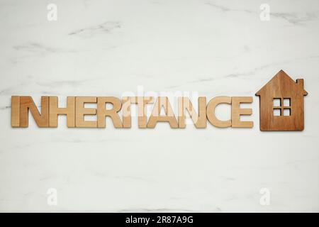 Wortvererbung mit Holzbuchstaben und Hausmodell auf weißem Marmorhintergrund, flach liegend Stockfoto