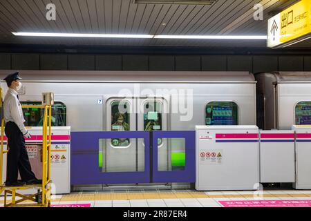 Mitarbeiter des U-Bahnnetzes von Tokio, Zugwächter an einer Station, während Pendler warten, um aus dem Zug auszusteigen, Tokio, Japan, 2023 Stockfoto