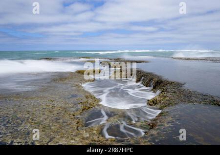 Gezeitenbecken, die bei Ebbe freigelegt werden und kleine Mini-Wasserfälle erzeugen Stockfoto