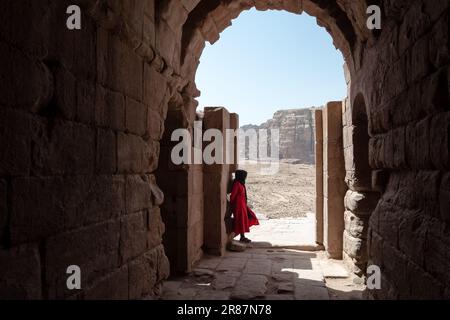 Eine einsame Frau in Rot, die auf die Wüstenberge von Petra im südlichen Jordanien starrt, in dem Tal, das vom Toten Meer bis t verläuft Stockfoto