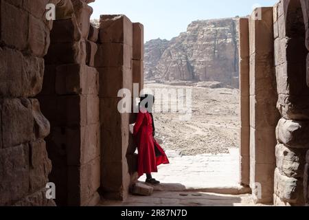 Eine einsame Frau in Rot, die auf die Wüstenberge von Petra im südlichen Jordanien starrt, in dem Tal, das vom Toten Meer bis t verläuft Stockfoto