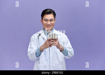 Porträt eines Arztes mit Handy und Lächeln isoliert über lila Hintergrund. Stockfoto