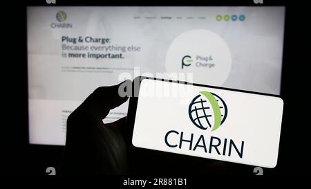 Person, die ein Mobiltelefon mit dem Logo der globalen CharIN e.V. auf dem Bildschirm vor der geschäftlichen Webseite hält. Konzentrieren Sie sich auf das Display des Telefons. Stockfoto
