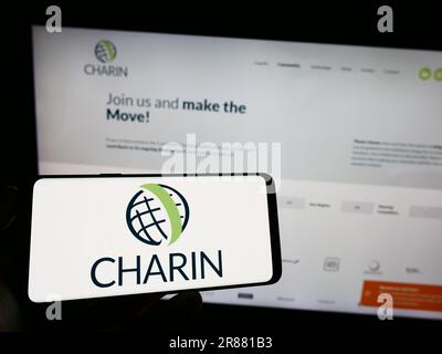 Person, die ein Mobiltelefon mit dem Logo der globalen CharIN e.V. auf dem Bildschirm vor der Webseite hält. Konzentrieren Sie sich auf das Display des Telefons. Stockfoto