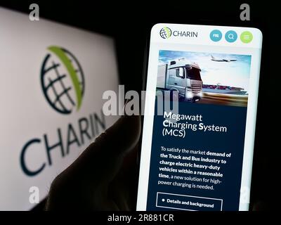 Person, die ein Mobiltelefon mit der Webseite der globalen CharIN e.V. auf dem Bildschirm vor dem Logo hält. Konzentrieren Sie sich auf die Mitte des Telefondisplays. Stockfoto