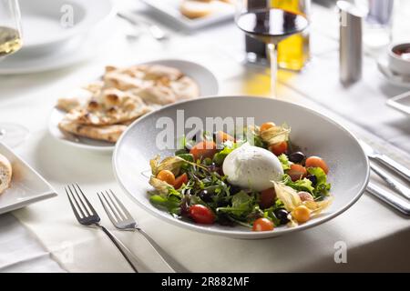 Italienischer Salat mit einer Kugel Buffalo Mozzarella in der Mitte serviert auf einem Teller mit einem Flachbildschirm und Rotwein. Stockfoto