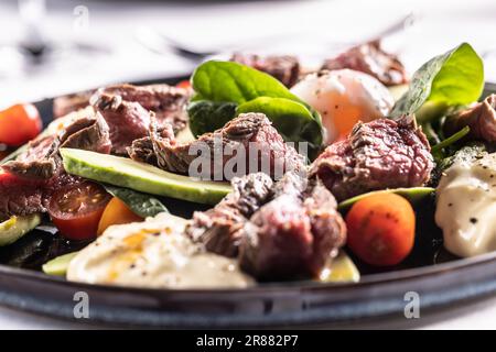 Paleo-Diät mit Flankensteak, Spinatblättern, Avocado, Tomaten, Eiern und Basilikumblättern auf einem Teller. Stockfoto