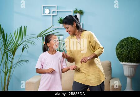 Fröhliche indische Mutter mit Tochter, die zu Hause tanzt - Konzept von Vergnügen, Familienbeziehung und sorgenfreiem Lebensstil Stockfoto