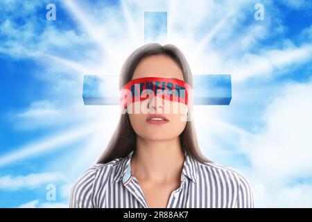 Eine Frau mit roten Augen und dem Wort Atheismus, Himmel mit Wolken und Kreuzsilhouette im Hintergrund Stockfoto