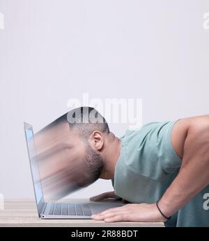 Internetsucht. Junger Mann, der sich am Tisch in einem Laptop auflöst Stockfoto
